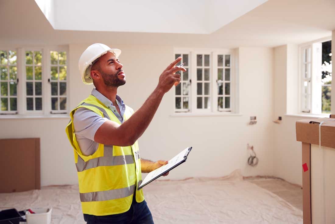 Building Surveyor Wearing Hard Hat With Clipboard Looking At Interior Of New Property House Inspection Engineer